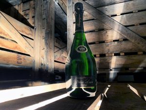 Photographie, intérieur. Une bouteille de champagne de la cuvée Prestige est mise en avant dans un décor ambiance cave. Texte étiquette : Champagne Didier Lapie Prestige
