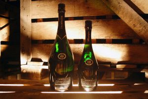 Photographie, intérieur. 2 bouteilles de champagne de la cuvée prestige : une classique (75cl) et une Magnum (150cl). Textes étiquettes : Champagne Didier Lapie Prestige